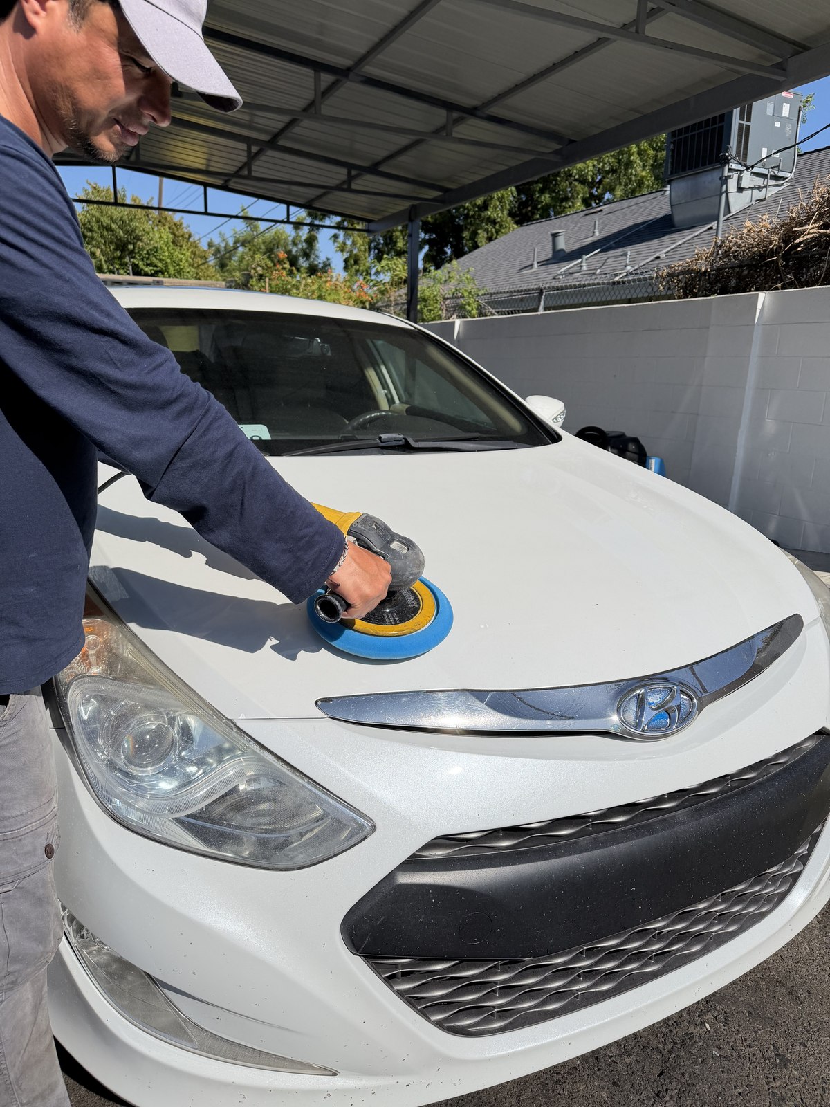 Detailer using a dual-action polisher on a car hood